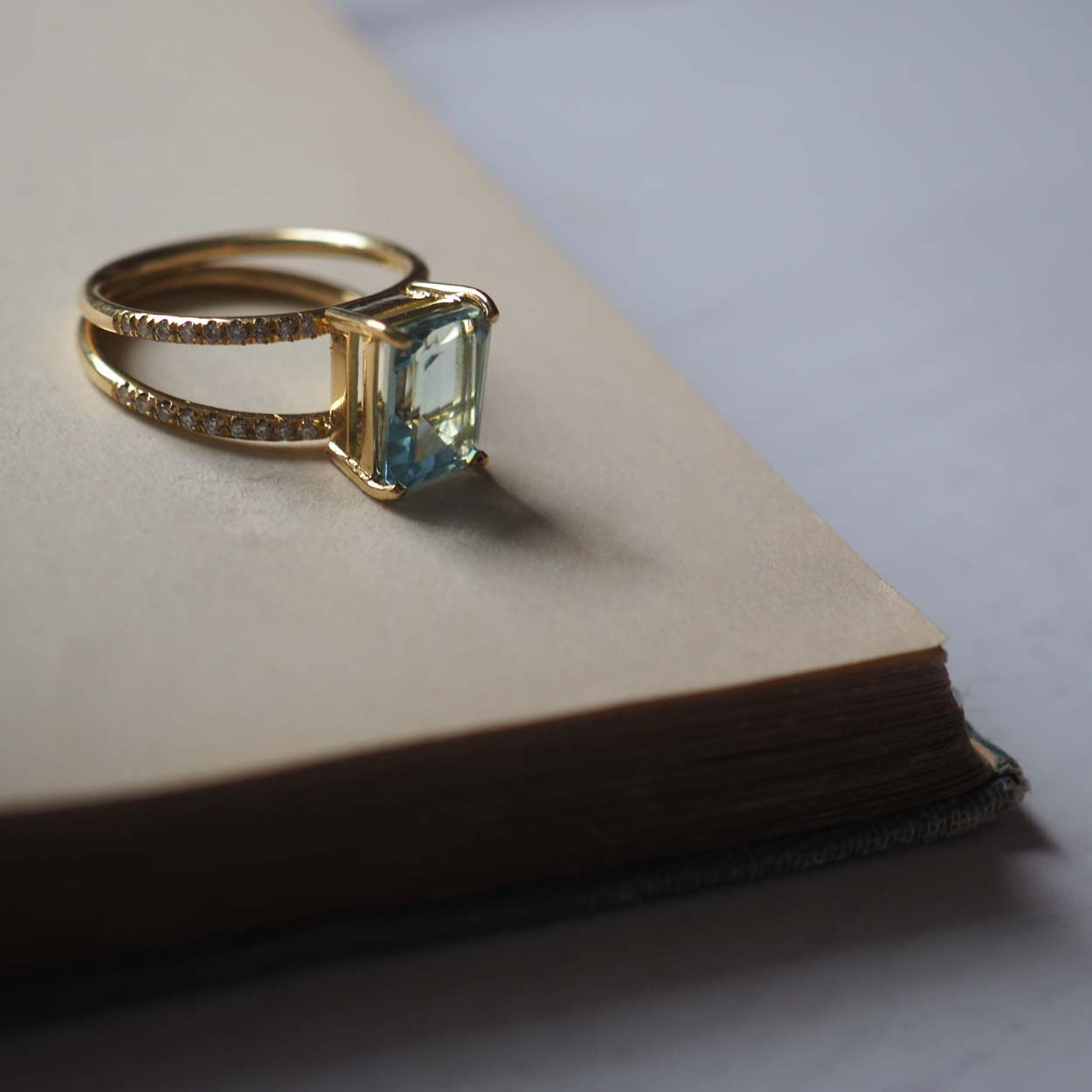 Elegant Emerald-Cut Aquamarine Ring by Bianca Jones Jewellery, handcrafted in London. Features a striking aquamarine stone set on dual gold bands, each adorned with sparkling diamonds.