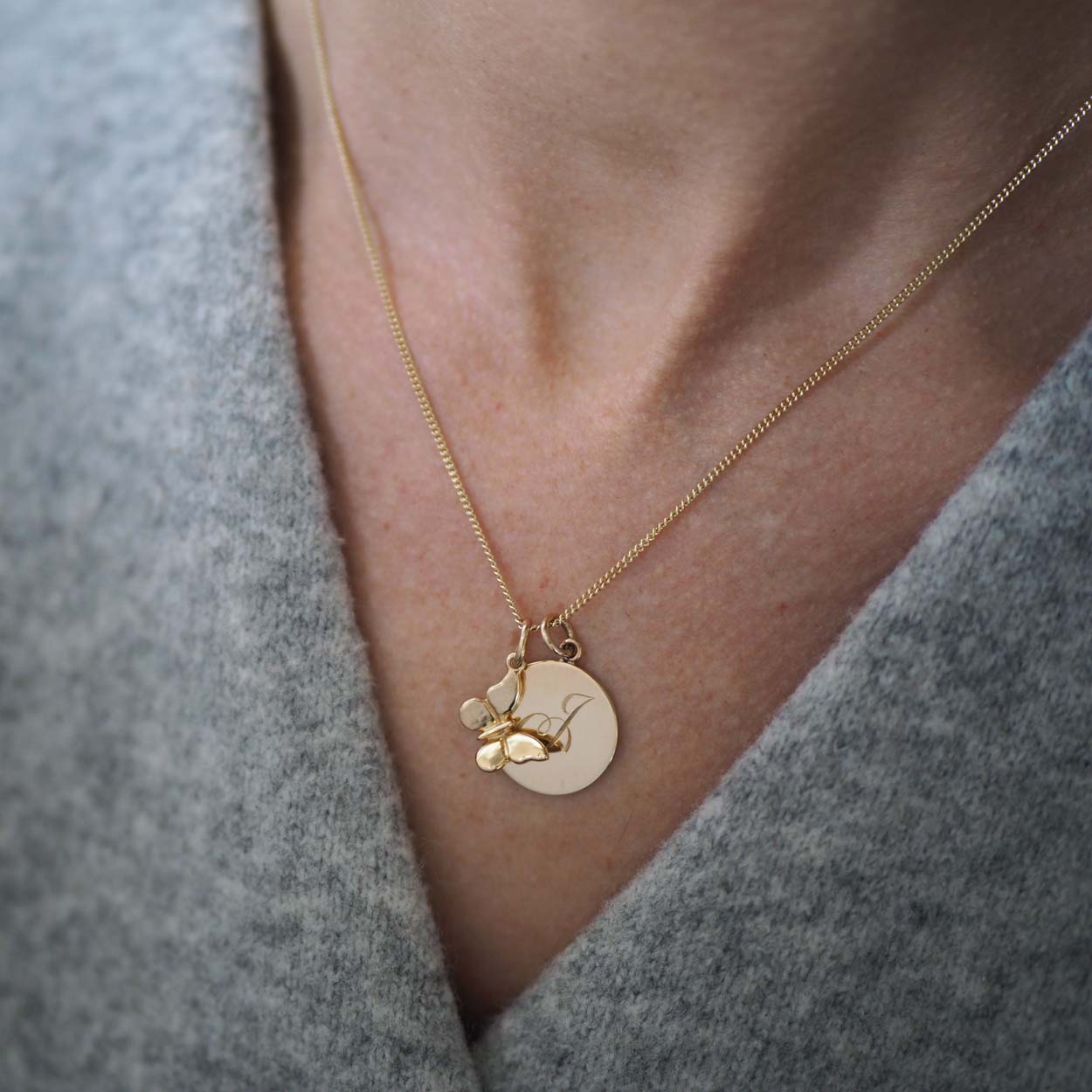 Bianca Jones handmade solid 9ct gold butterfly charm featuring intricate detailing is seen on a chain with a hand-engraved initial disc charm in rose, white, or yellow gold.