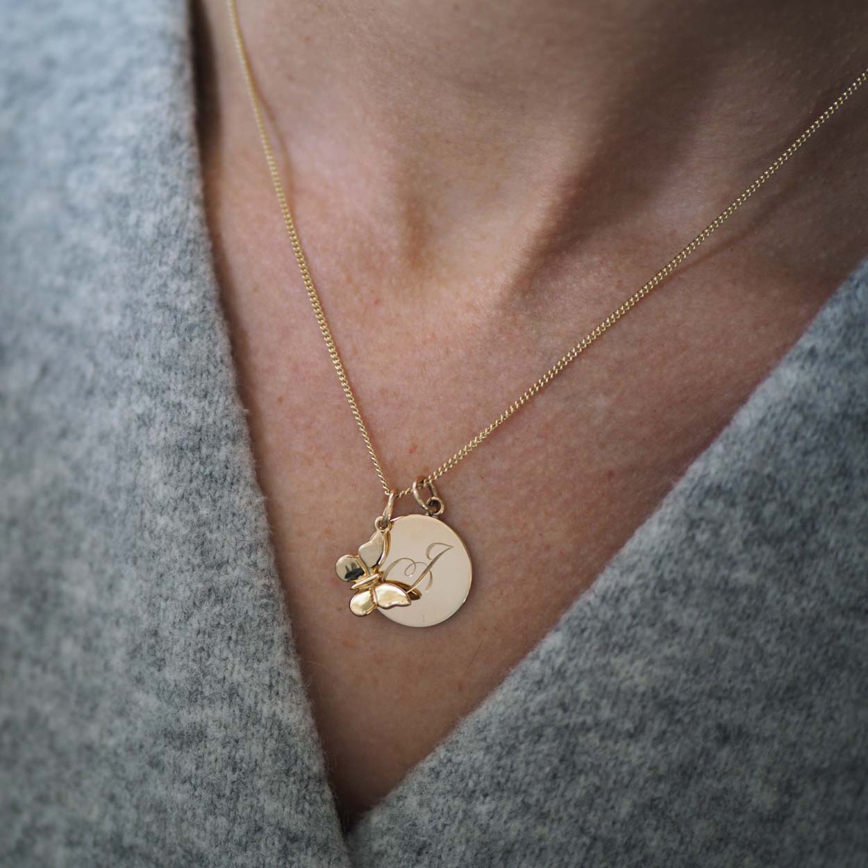 Bianca Jones handmade solid 9ct gold butterfly charm featuring intricate detailing is seen on a chain with a hand-engraved initial disc charm in rose, white, or yellow gold.