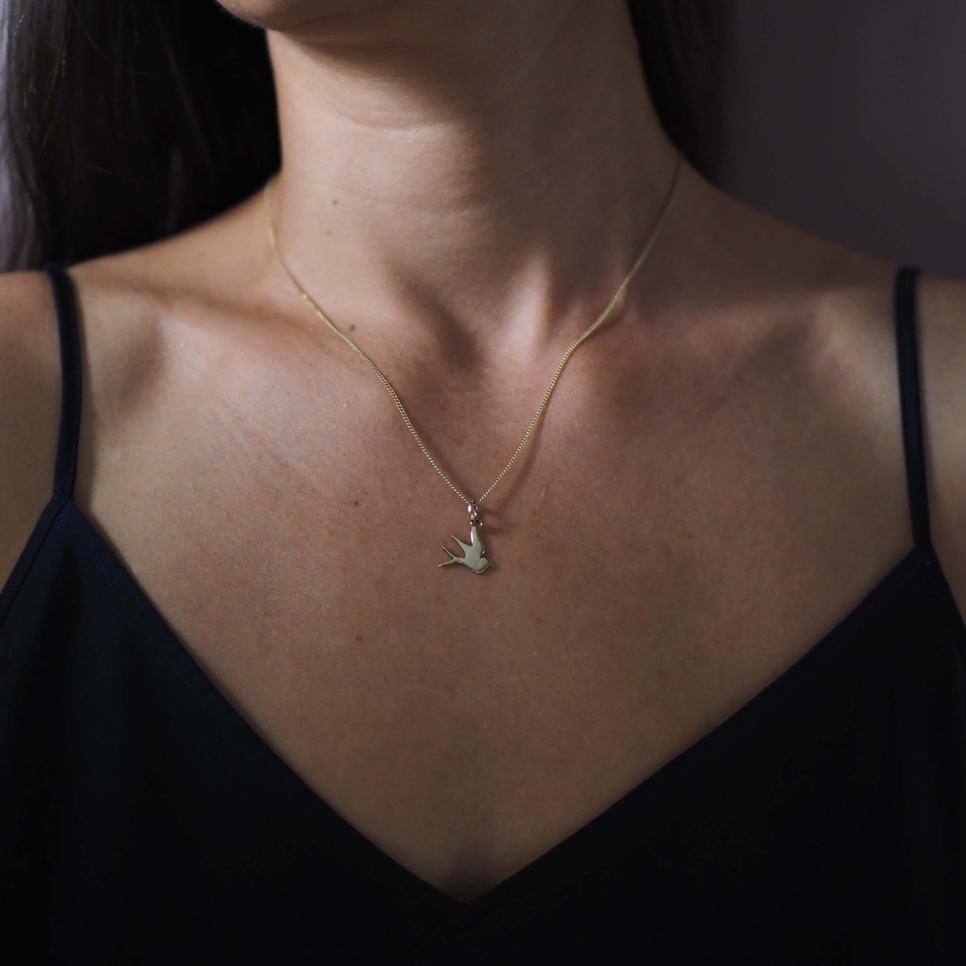 Solid gold swallow necklace on model – handcrafted talisman symbolising hope, love, and safe return