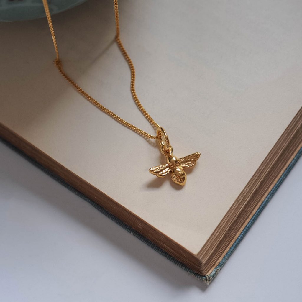18ct gold bee necklace on fine chain, flatlay jewellery photo on a book