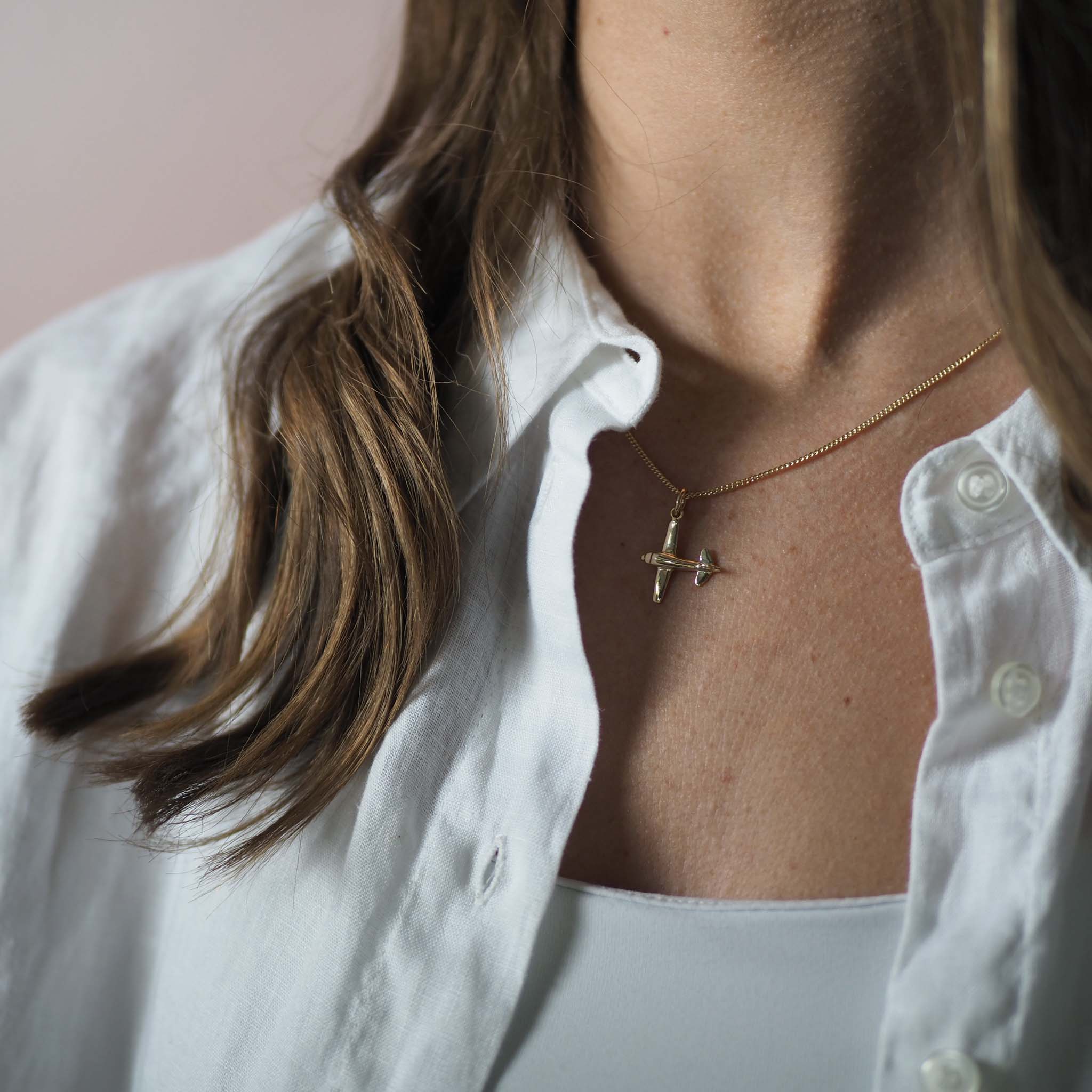 Woman wearing 9ct solid gold airplane necklace layered with other gold jewellery
