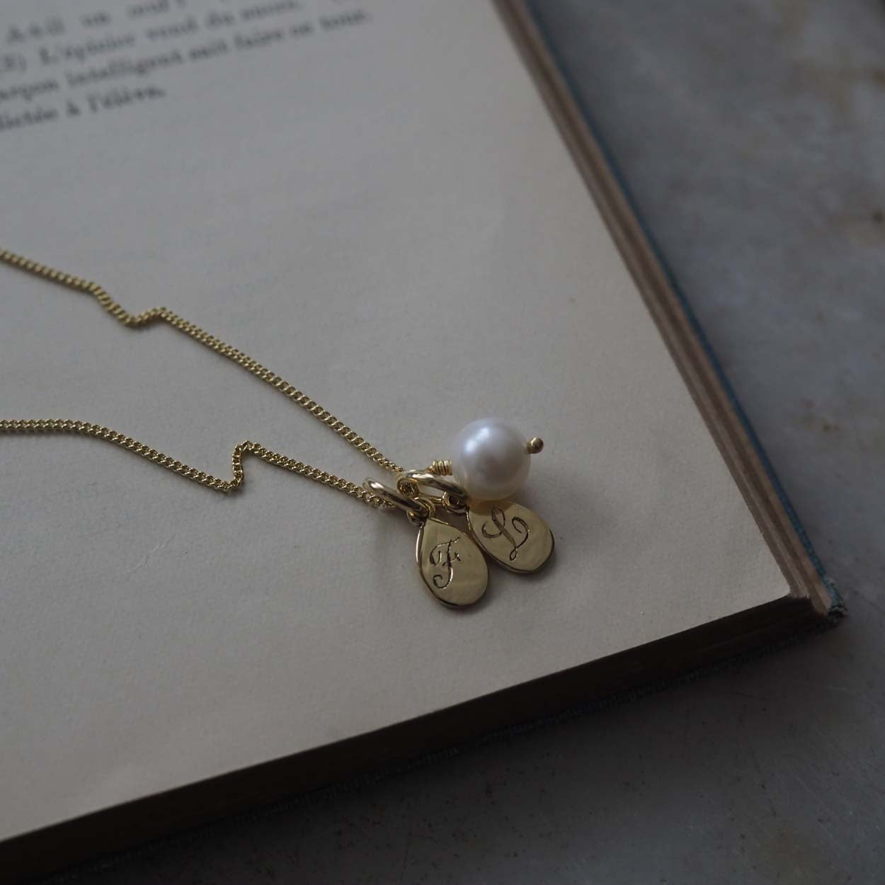 Double Teardrop Initial and Pearl Necklace in Solid Gold with two engraved teardrop pendants and a pearl charm. A timeless piece symbolizing love and cherished connections.