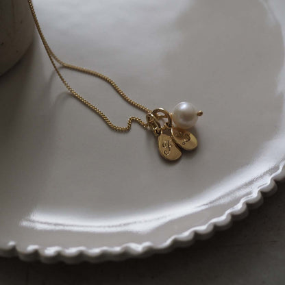 Double Teardrop Initial and Pearl Necklace in Solid Gold with two engraved teardrop pendants and a pearl charm. A timeless piece symbolizing love and cherished connections.