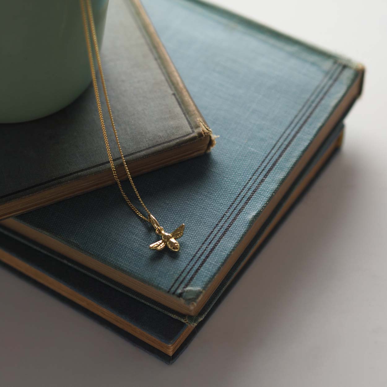 18ct gold bee necklace on fine chain, flatlay jewellery photo, on stacked books 