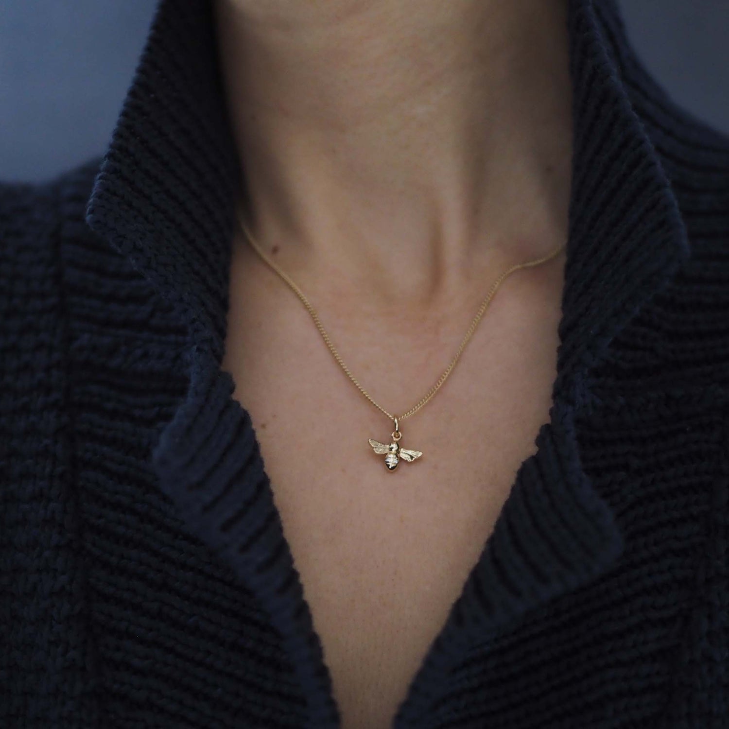 Model wearing 18ct gold bee necklace on 18-inch chain with a blue cardigan 