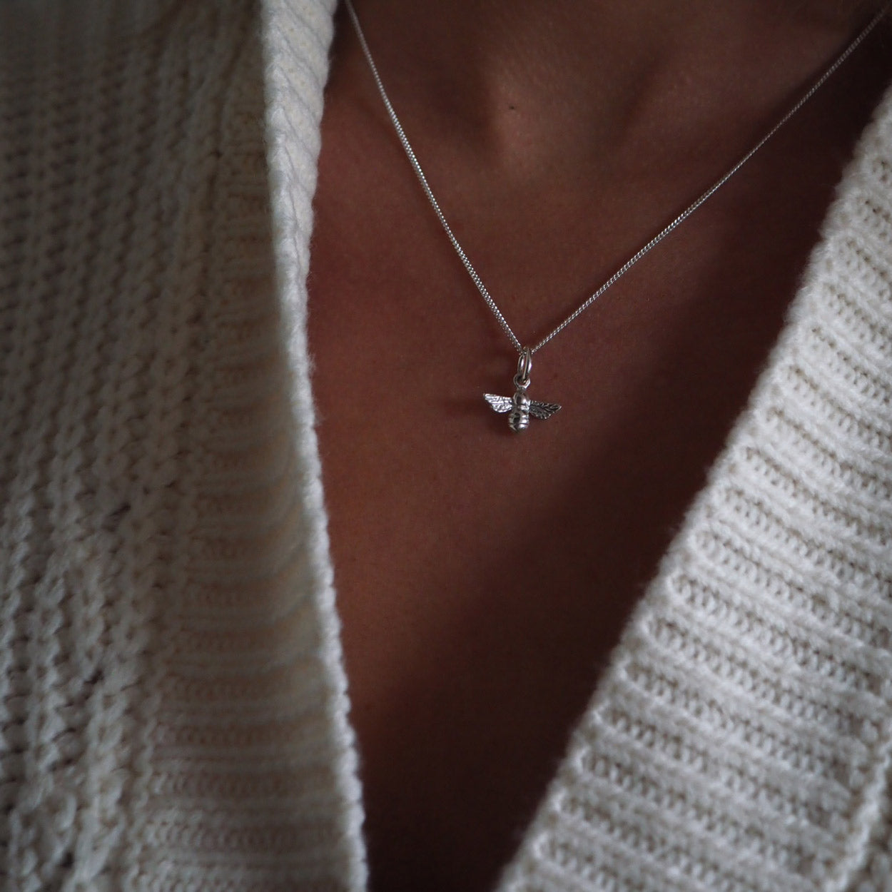 Model wearing sterling silver bee necklace on a 16-inch chain and a white cardigan