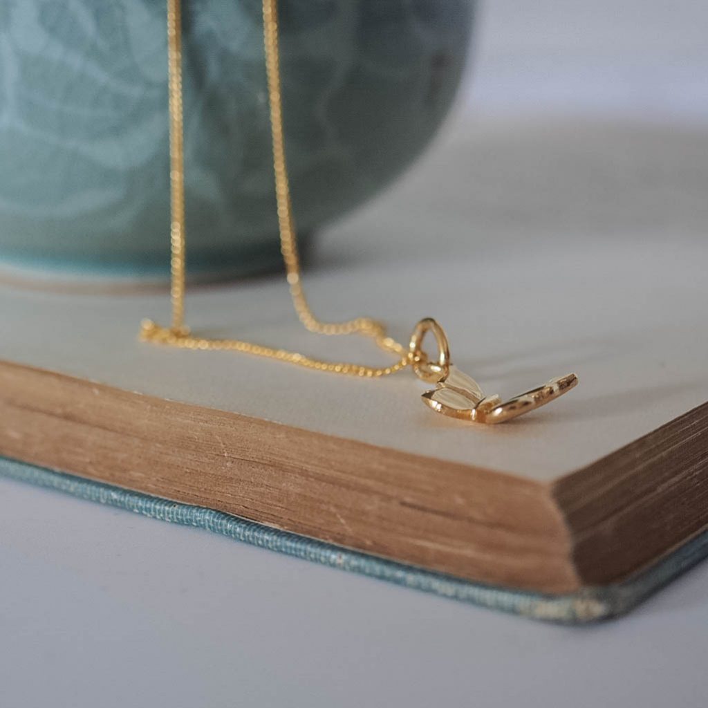 Delicate solid gold butterfly pendant, symbolising transformation and renewal, shown from the side and close up