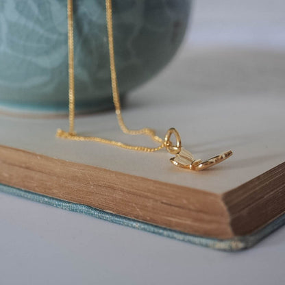 Delicate solid gold butterfly pendant, symbolising transformation and renewal, shown from the side and close up