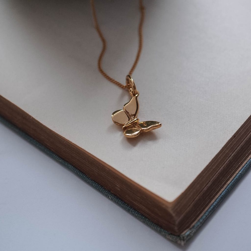 Delicate solid gold butterfly pendant, symbolising transformation and renewal, shown from the side