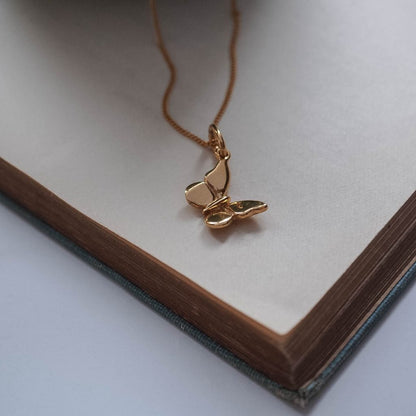 Delicate solid gold butterfly pendant, symbolising transformation and renewal, shown from the side